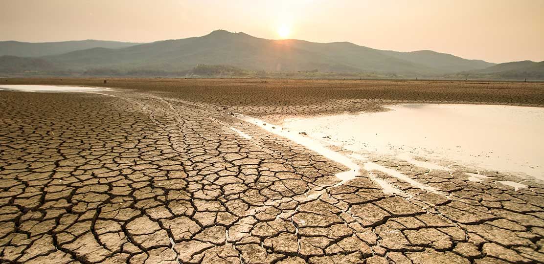 Tierra reseca, junto a unas lagunas y cerros al fondo.