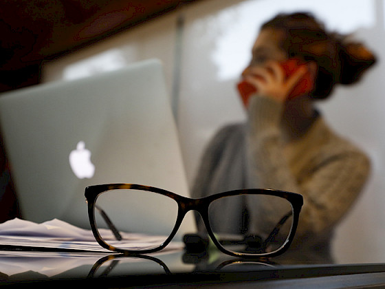 Foto de una alumna hablando por teléfono y trabajando frente a un computador.