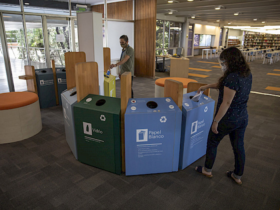Foto que muestra receptáculos coloridos de reciclaje de papel y otros materiales en la biblioteca San Joaquín del campus homónimo.