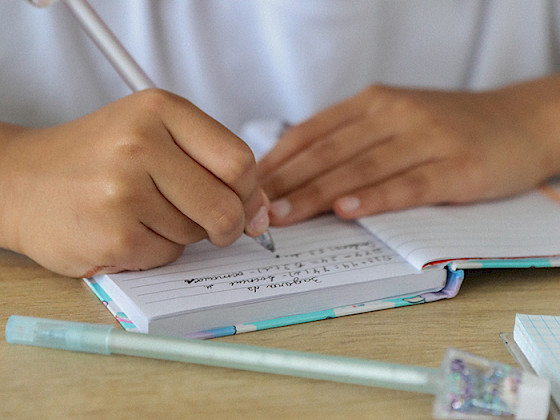 Manos de niño escolar escribiendo sobre un cuaderno.