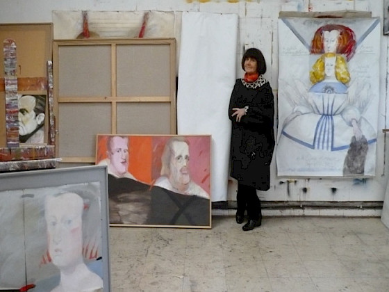 Retrato de Claudia Campaña a la fallecida artista Roser Bru, en el año 2009. Posando de pie, ropa negra, brazos cruzados, junto a sus cuadros, en medio de su taller.