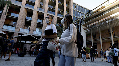 Pareja con mascarilla caminando por el patio de la Facultad de Comunicaciones.