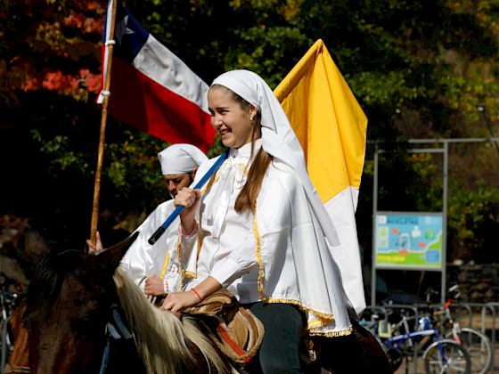 mujer con velo y llevando bandera del vaticano, montada en un caballo