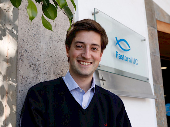 hombre joven sonriendo, detrás suyo hay un letrero que dice Pastoral UC