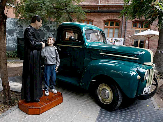 estatua de padre hurtado dándole la mano a un niño, al lado de una camioneta verde