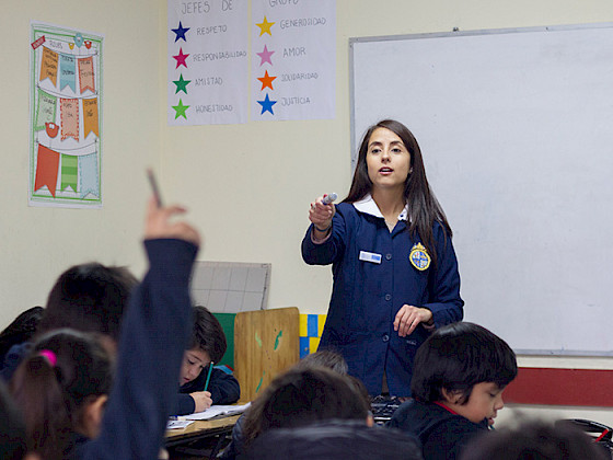 Profesora dando la palabra a una niña con la mano levantada.