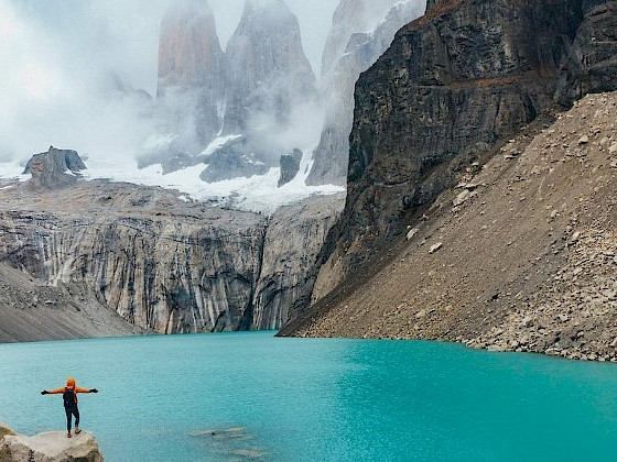 Persona con sus brazos abiertos mira el lago y al fondo las Torres del Paine.