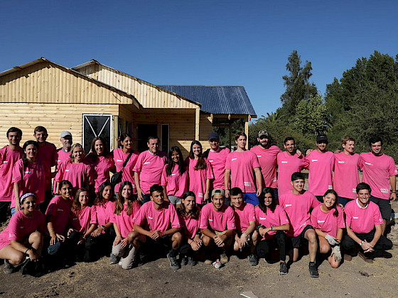 Grupo de jóvenes con poleras rosadas adelante de una casa