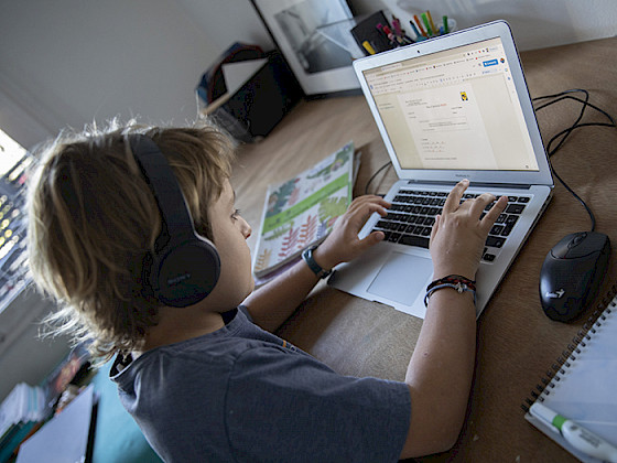 Niño con audífonos escribiendo en un computador.