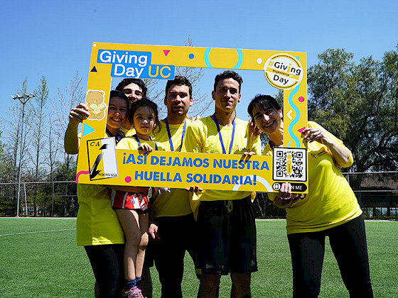 Grupo de personas usando polera amarilla y posando en un marco de Giving Day en una cancha de fútbol.