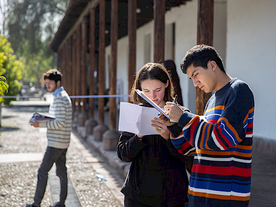 Dos jóvenes, hombre y mujer, anotan en sus cuadernos de pie en un patio.