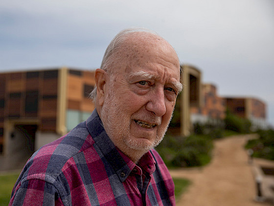 Fotografía de retrato de Juan Carlos Castilla con la Estación Costera de Investigaciones Marinas de fondo.