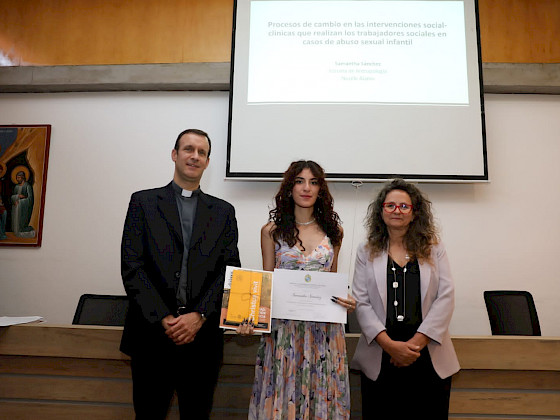 tres personas de pie, una de ellas sostiene un diploma