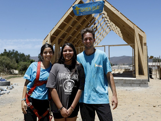 Voluntarios de misiones junto a una joven de la comunidad, de fondo luna capilla en construcción.