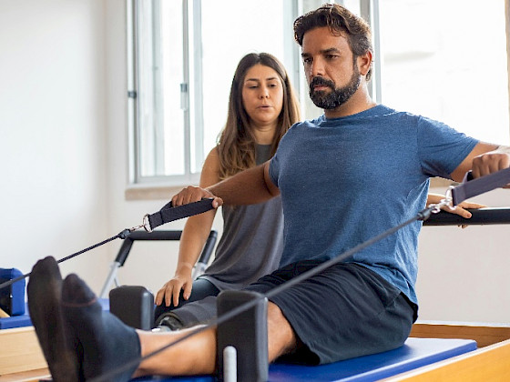 Hombre en ropa deportiva haciendo ejercicios con una mujer que lo observa al lado.