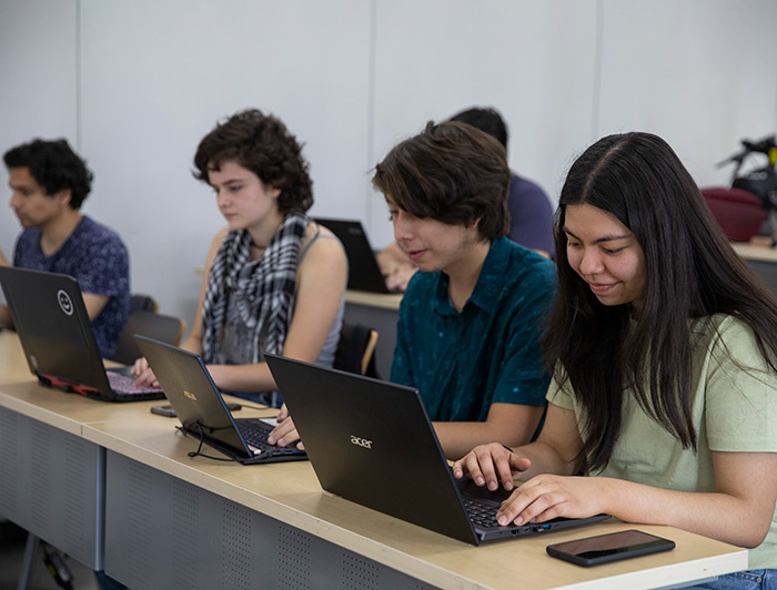 Estudiantes universitarios trabajando en sus computadores en una sala de clases.