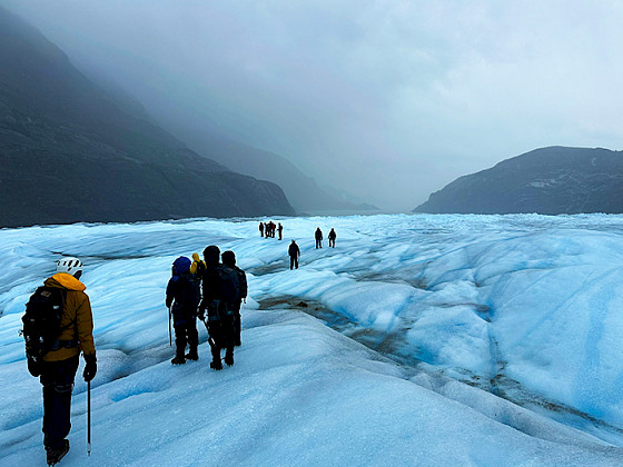 Grupo de personas sobre un glaciar con montañas de fondo.