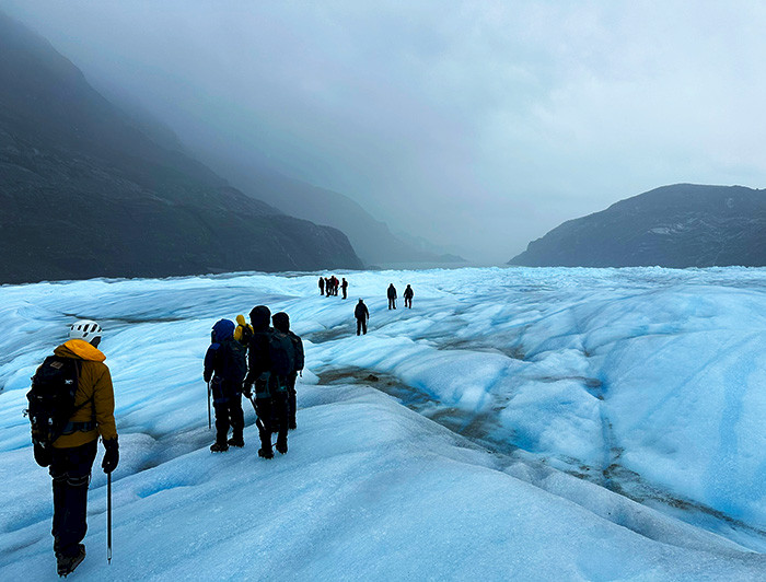 Grupo de personas sobre un glaciar con montañas de fondo.