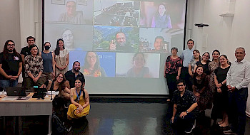 Grupo de participantes del Boot Camp de enero, en una sala de clases, junto a una pantalla con participantes online.