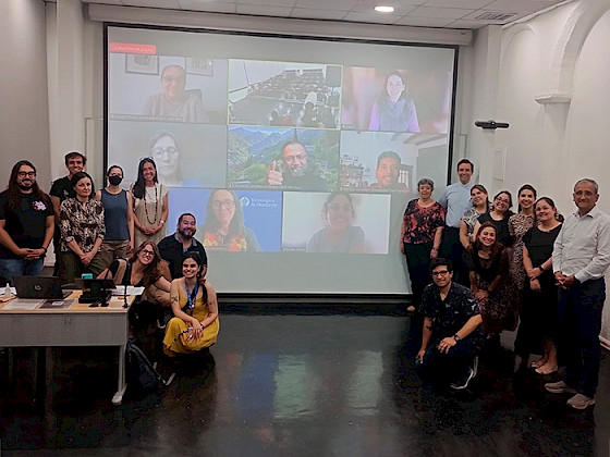 Grupo de participantes del Boot Camp de enero, en una sala de clases, junto a una pantalla con participantes online.