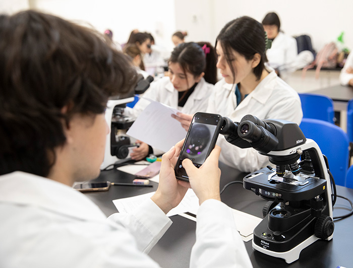 Un joven usa un celular con un microscopio en un laboratorio.