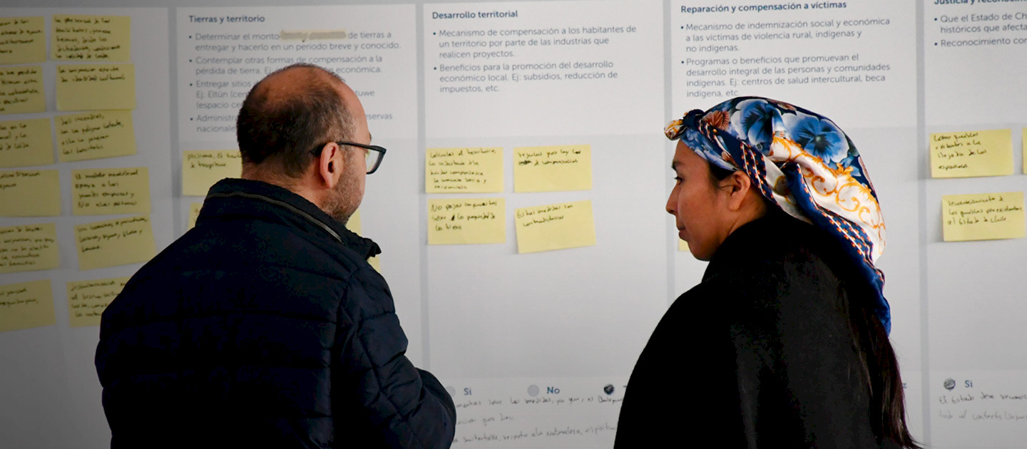 Un hombre y una mujer mapuche observan un papelógrafo con los resultados del diálogo intercultural.