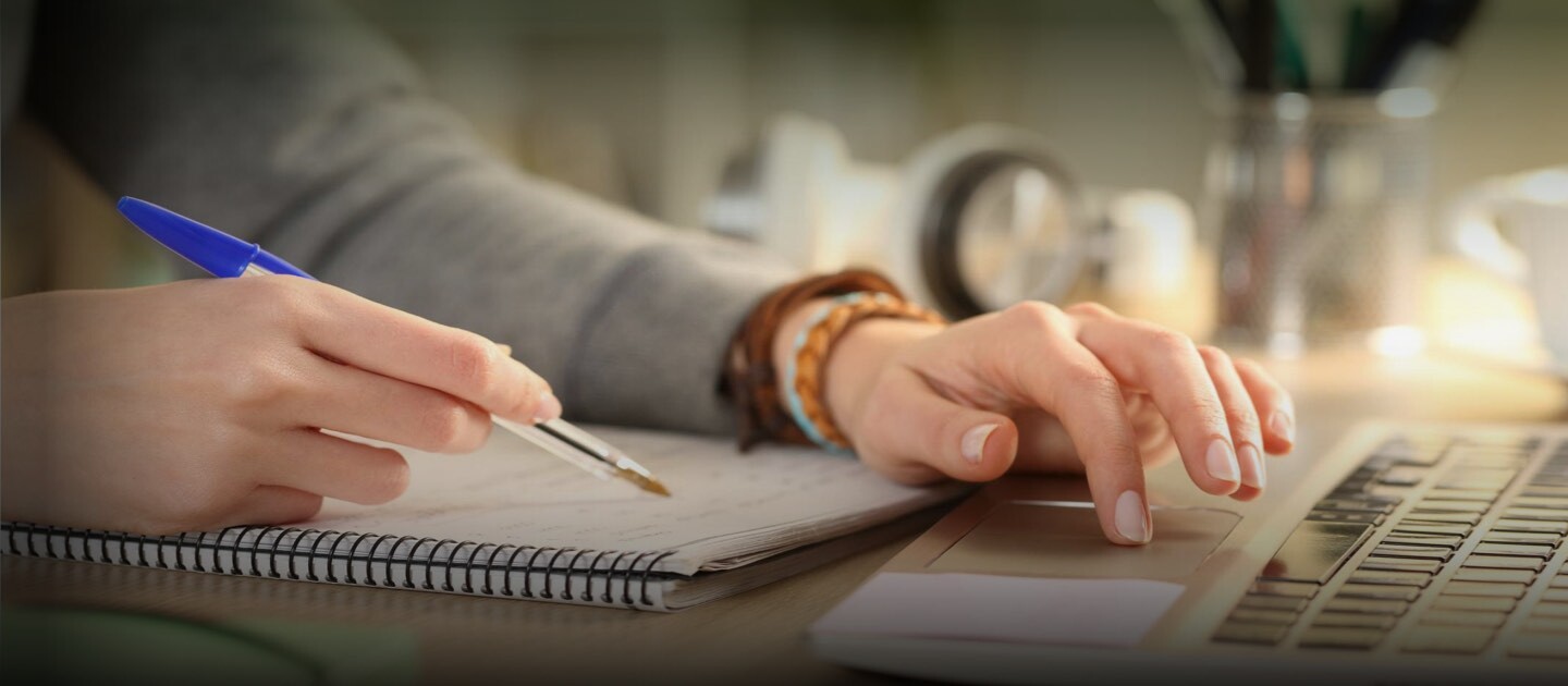 Manos de una persona escribiendo sobre un cuaderno y en el computador.