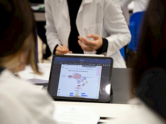 Una tablet muestra una figura de una mano humana, al rededor se ven siluetas de personas usando delantal blanco.