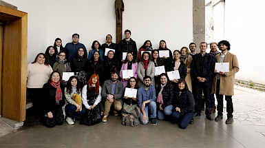 Grupo de Personas de pie, con diplomas en la mano, y un crucifijo en la muralla de atrás