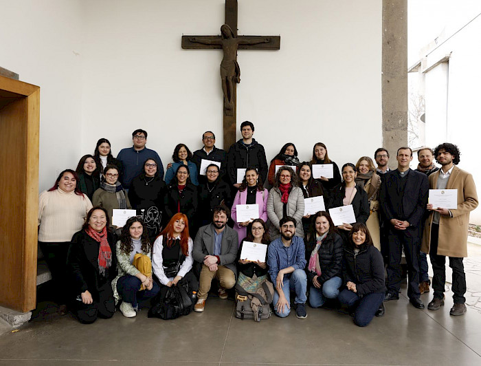 Grupo de Personas de pie, con diplomas en la mano, y un crucifijo en la muralla de atrás