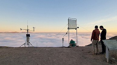 Dos jóvenes en terreno junto a instrumentos en un lugar árido y niebla de fondo