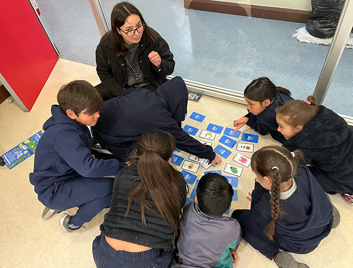 Escolares juegan con cartas junto a una monitora.