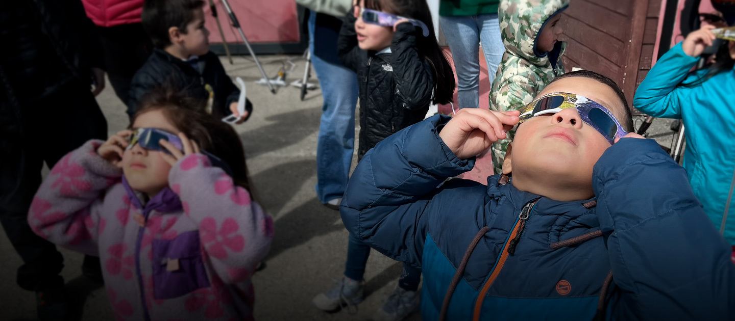 Niños observan el cielo con lentes especiales para ver un eclipse.