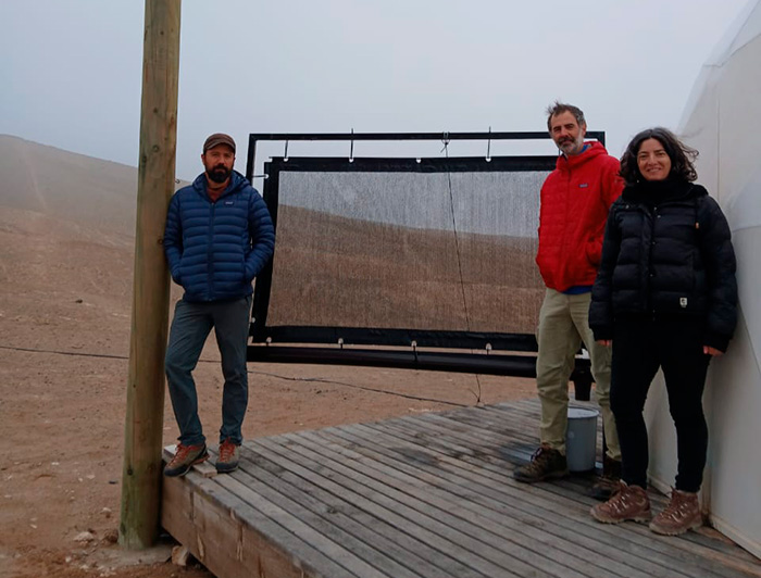 Los investigadores del Centro UC Desierto de Atacama Virginia Carter, Camilo del Río y Felipe Lobos junto a un atrapanieblas a escala. 