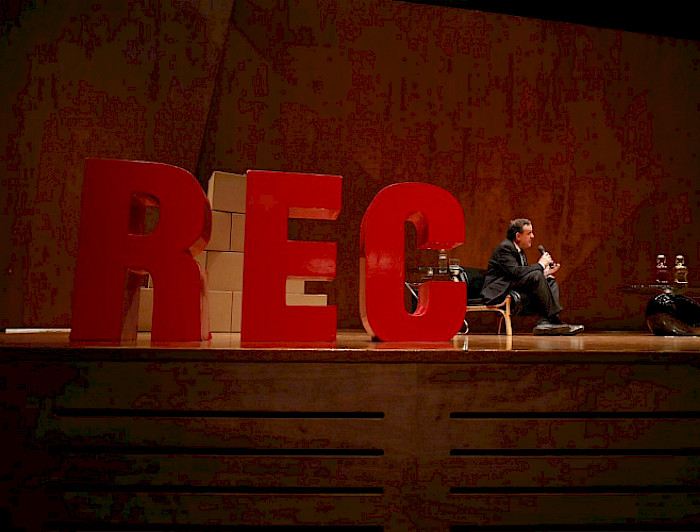 Letras R, E y C en grande y color rojo sobre un escenario