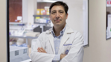 Dr. Alexis Kalergis, immunologist and professor at UC Chile, standing with arms crossed in a laboratory setting.