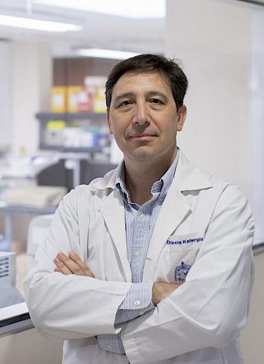 Dr. Alexis Kalergis, immunologist and professor at UC Chile, standing with arms crossed in a laboratory setting.