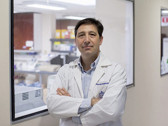 Dr. Alexis Kalergis, immunologist and professor at UC Chile, standing with arms crossed in a laboratory setting.