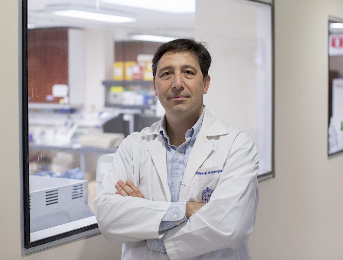 Dr. Alexis Kalergis, immunologist and professor at UC Chile, standing with arms crossed in a laboratory setting.