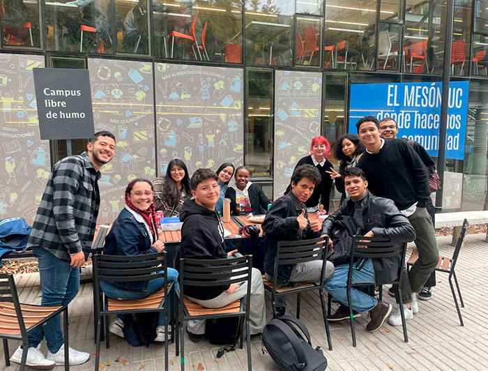 Grupo de estudiantes de la Red de Alumnos/as Extranjeros/as (RAE) de la UC, sentados en unas mesas en el patio.