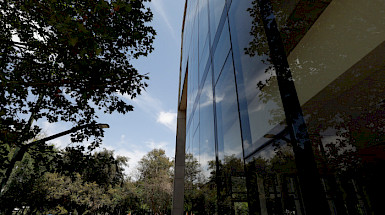 View of UC Chile’s School of Business building at the San Joaquín Campus, with reflections on the windows and trees in the background.