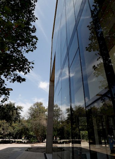 View of UC Chile’s School of Business building at the San Joaquín Campus, with reflections on the windows and trees in the background.