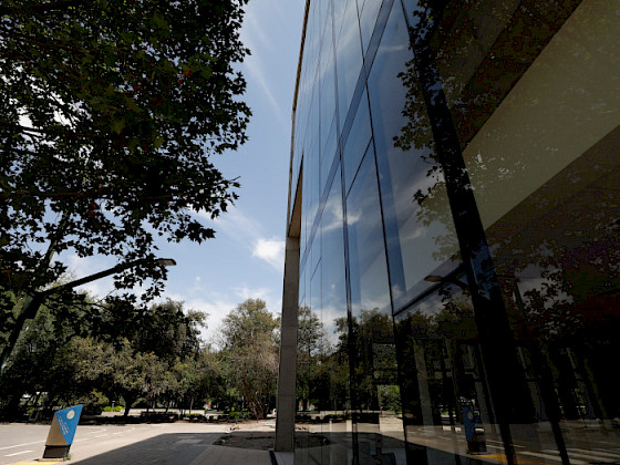 View of UC Chile’s School of Business building at the San Joaquín Campus, with reflections on the windows and trees in the background.