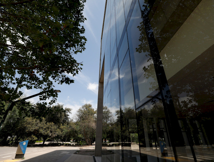 View of UC Chile’s School of Business building at the San Joaquín Campus, with reflections on the windows and trees in the background.