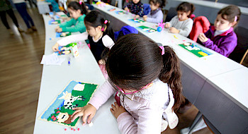 Niñas y niños haciendo trabajos de artes plásticas en una sala.