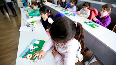 Niñas y niños haciendo trabajos de artes plásticas en una sala.