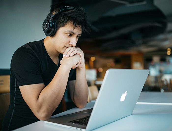 Hombre joven frente a una mesa y un computador portátil.