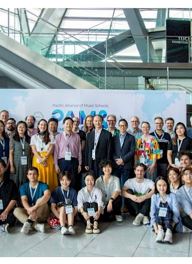 A diverse group of music educators, students, and professionals pose for a group photo at the Pacific Alliance of Music Schools event in a modern conference setting. (Photo credit: IMUC-PAMS)