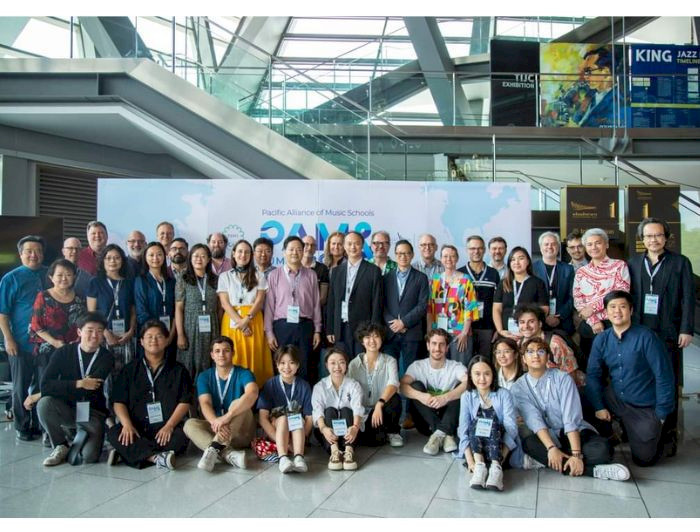 A diverse group of music educators, students, and professionals pose for a group photo at the Pacific Alliance of Music Schools event in a modern conference setting. (Photo credit: IMUC-PAMS)