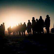 Siluetas de migrantes caminando al atardecer.